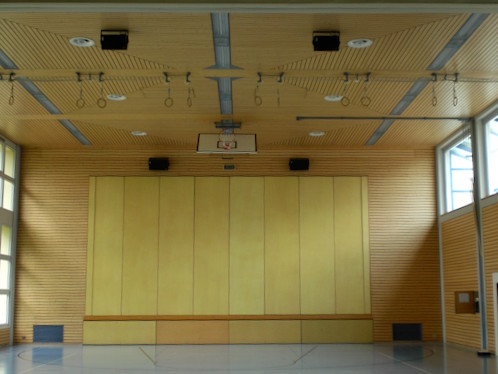 Turnhalle mit fest installierten Wandlautsprechern und moderner Holzverkleidung für gleichmässige Raum­beschallung