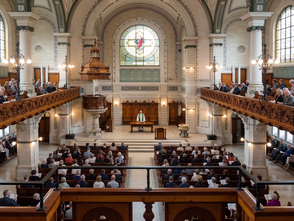Kirche Rohrbach – professionelle Kirchenbeschallung für klare Sprachverständlichkeit Innenraum der Kirche Rohrbach mit voll besetzter Gemeinde, Empore mit Musikerensemble und moderner Kirchenbeschallung; klare Sprachübertragung und ausgewogene Akustik für Gottesdienste und musikalische Aufführungen.