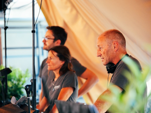 Technikteam betreut eine Veranstaltung im Hintergrund und arbeitet konzentriert an Ton- und Lichtsteuerung unter einem Eventzelt.