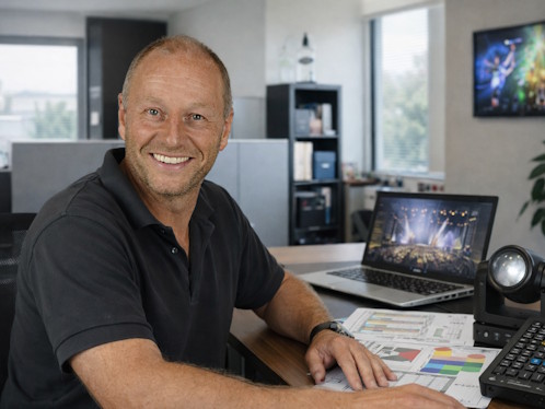 Eventberater im modernen Büro bei der Konzeptplanung: Laptop mit Eventlayout, technische Geräte wie Lichtsteuerung und Mischpult, freundliche Atmosphäre mit Tageslicht – professionelle Beratung für Events und Festinstallationen bei Manser Events